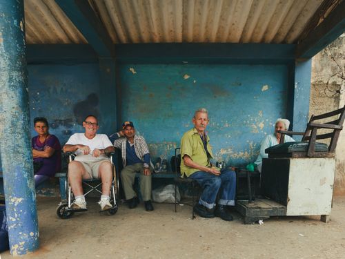 Free A group of elderly people sitting together outside under a rustic shelter, smiling and relaxed. Stock Photo