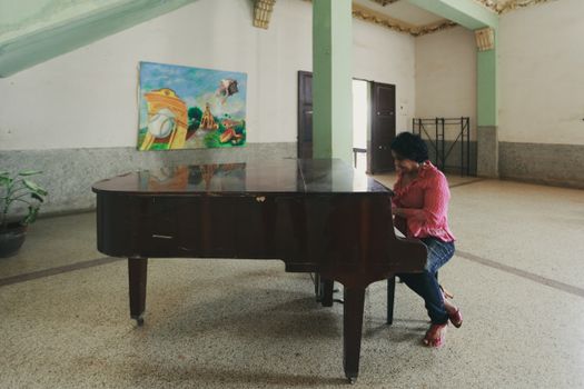 Woman playing grand piano indoors with artistic painting in background.