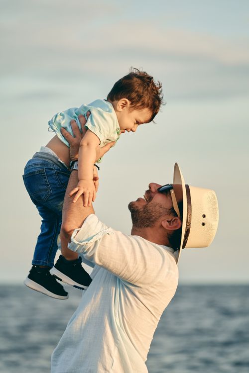 Free A joyful father lifting his smiling son by the ocean on a sunny day. Stock Photo