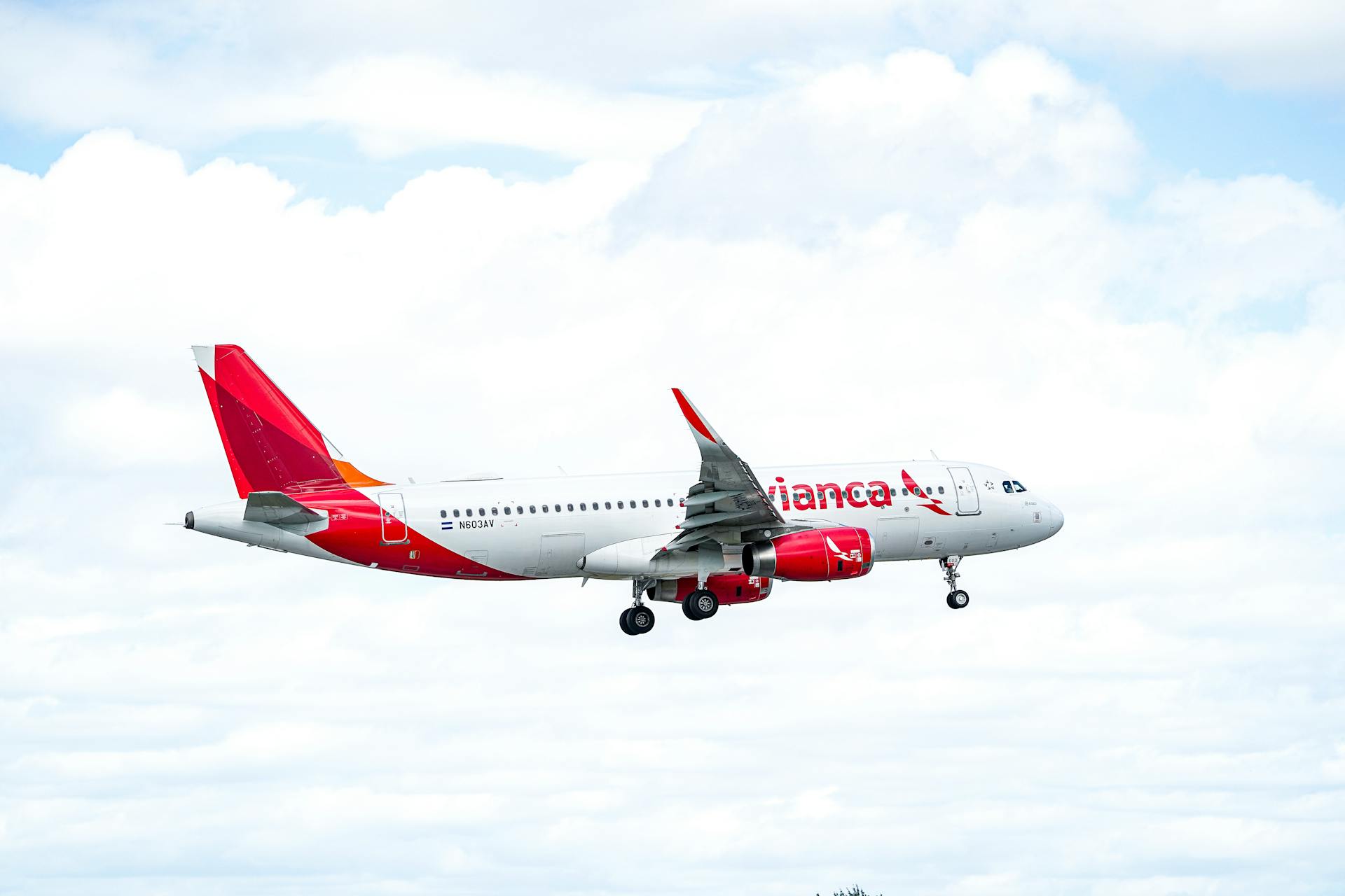 A commercial airliner with red accents flying against a backdrop of a cloudy sky.