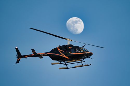 Free A helicopter silhouetted against a clear sky with the moon in the background, captured from below. Stock Photo