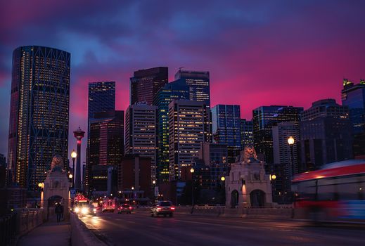 Stunning view of Calgary's illuminated skyline during a vibrant pink sunset, featuring skyscrapers and urban landscape.