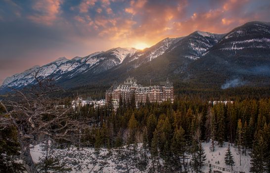 Scenic view of Banff Springs Hotel amid snow-covered mountains at sunset.