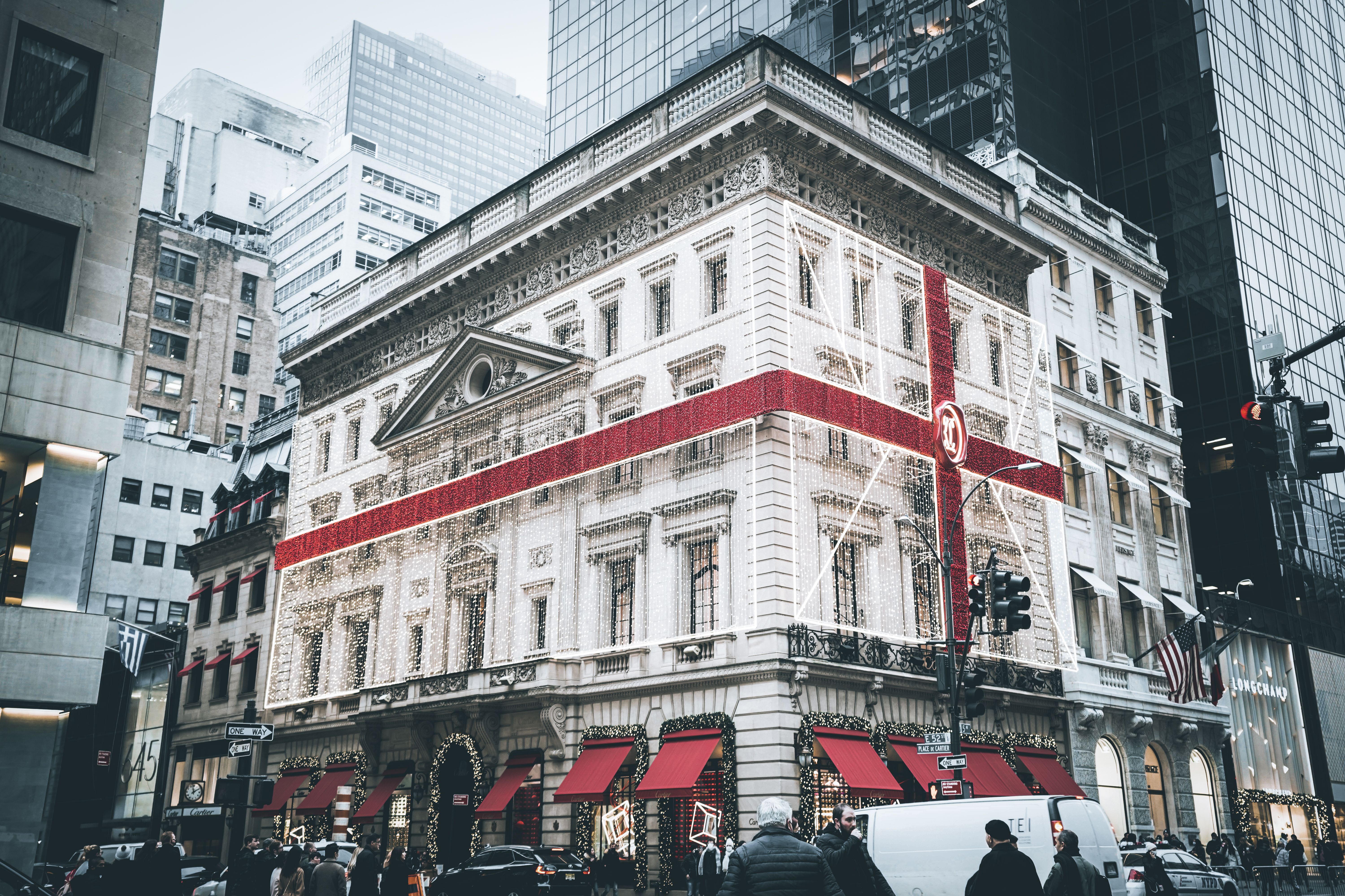 A beautifully decorated building with festive lights and a large red ribbon, set in a busy city street.