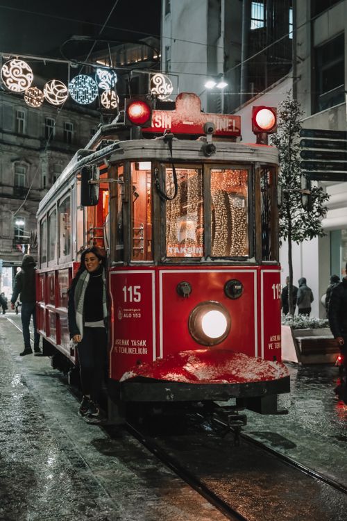 Free Woman standing by vintage red tram in a festive city street at night during winter. Stock Photo