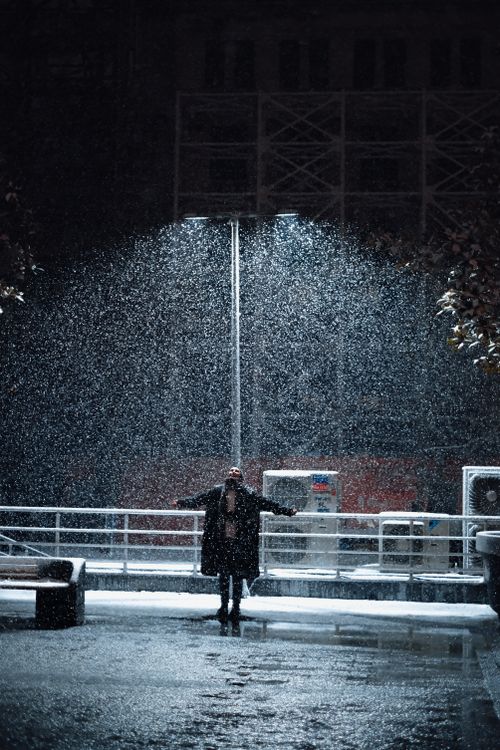Free Person stands under streetlight at night, surrounded by falling snow. Stock Photo