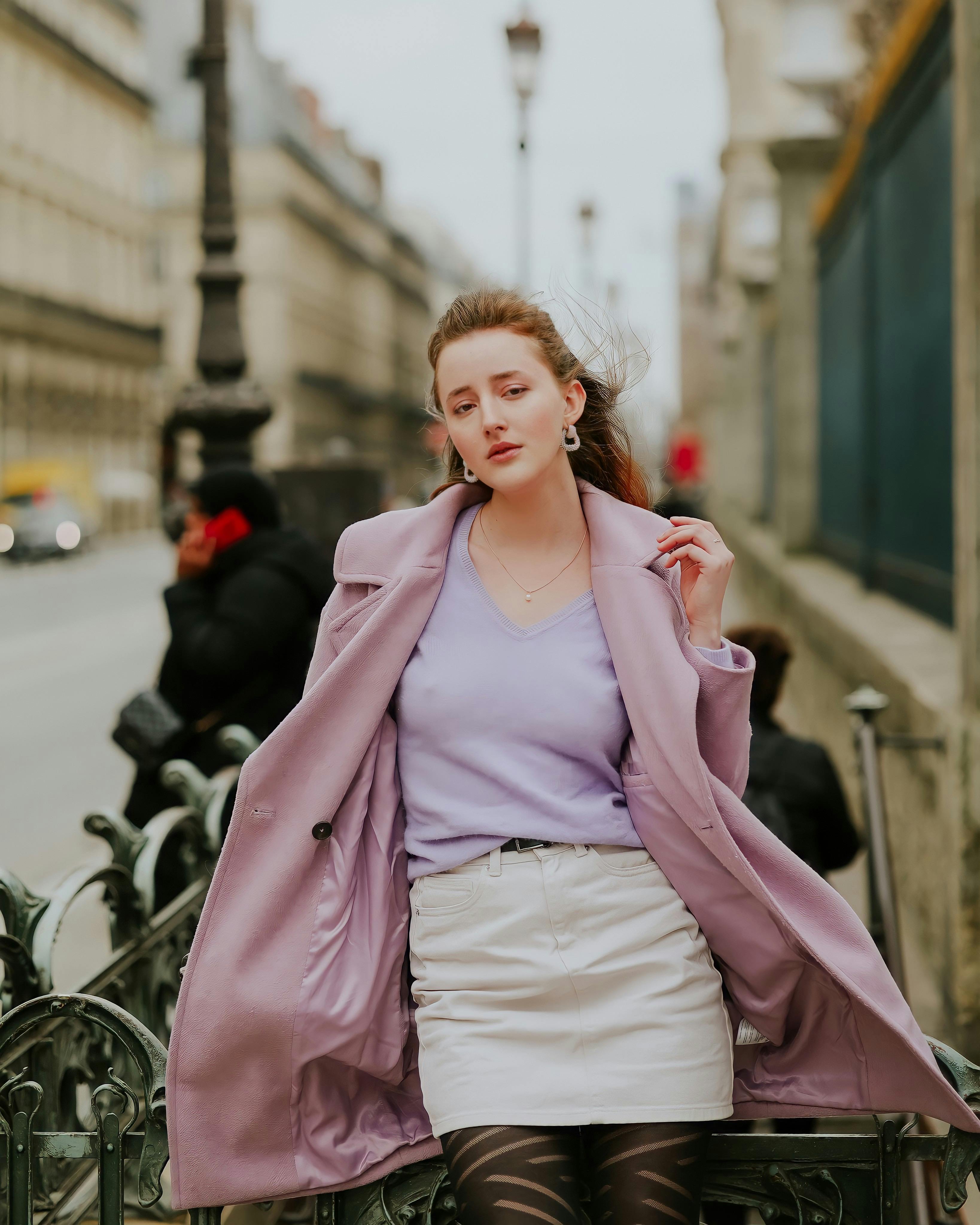 Elegant woman in lilac coat poses confidently on a Paris street, showcasing urban fashion.
