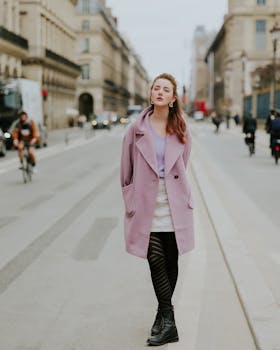 Woman in a fashionable pink coat and black boots strolling down a scenic urban street.