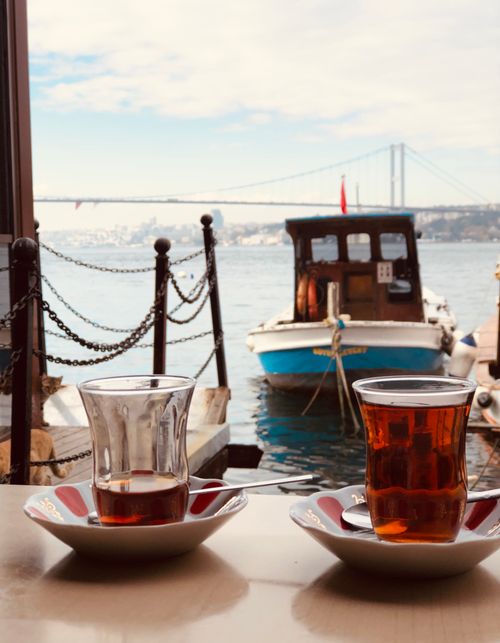 Free Enjoy traditional Turkish tea by the Bosphorus with a scenic view of a boat and the bridge in İstanbul. Stock Photo