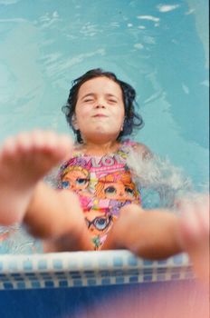 A joyful child splashes playfully in a swimming pool wearing a colorful swimsuit.