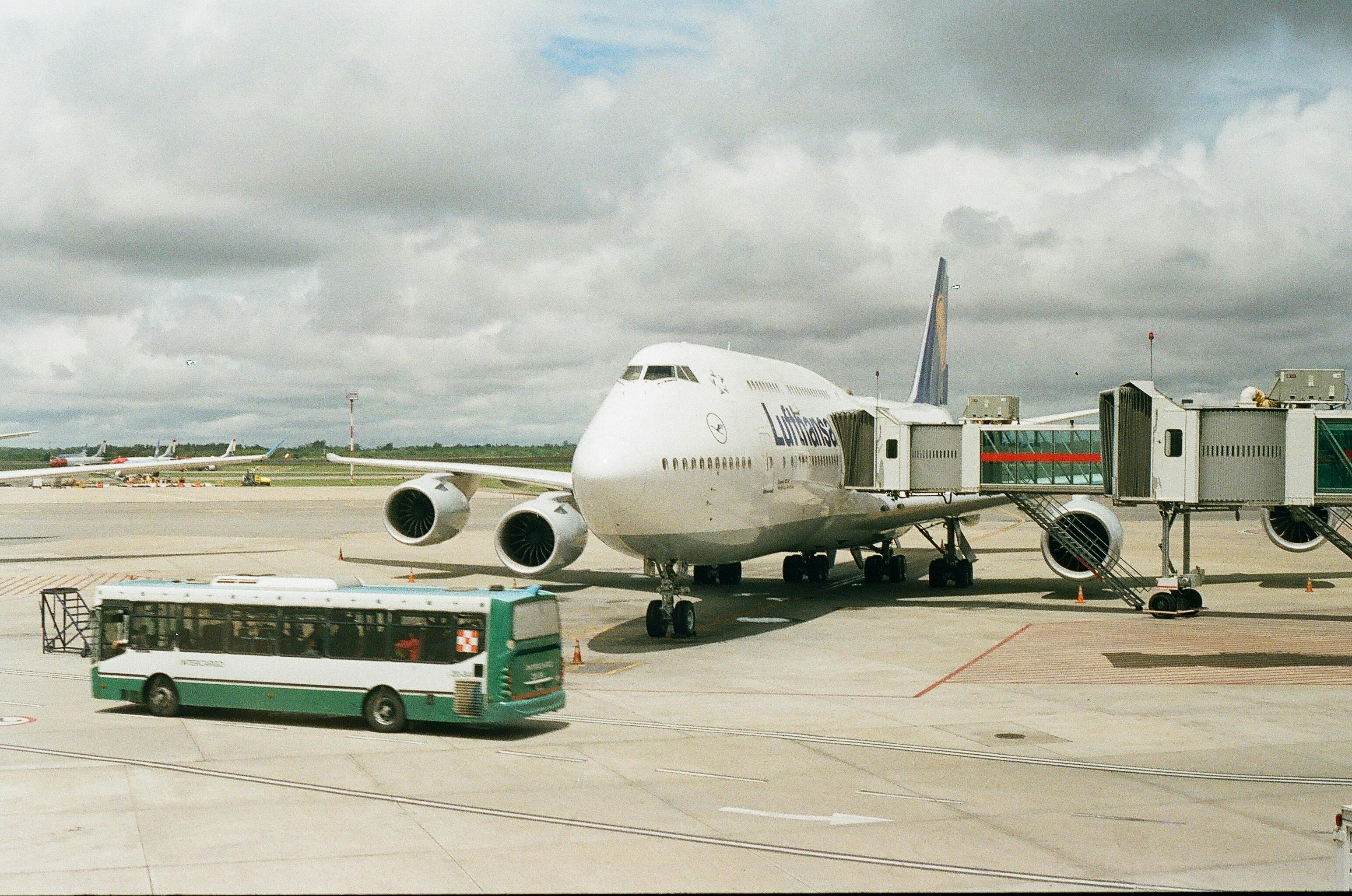 plane on airport with telescopic corridor attached and bus driving in front of it