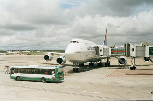 Free Plane on Airport with Telescopic Corridor Attached and Bus Driving in front of It Stock Photo