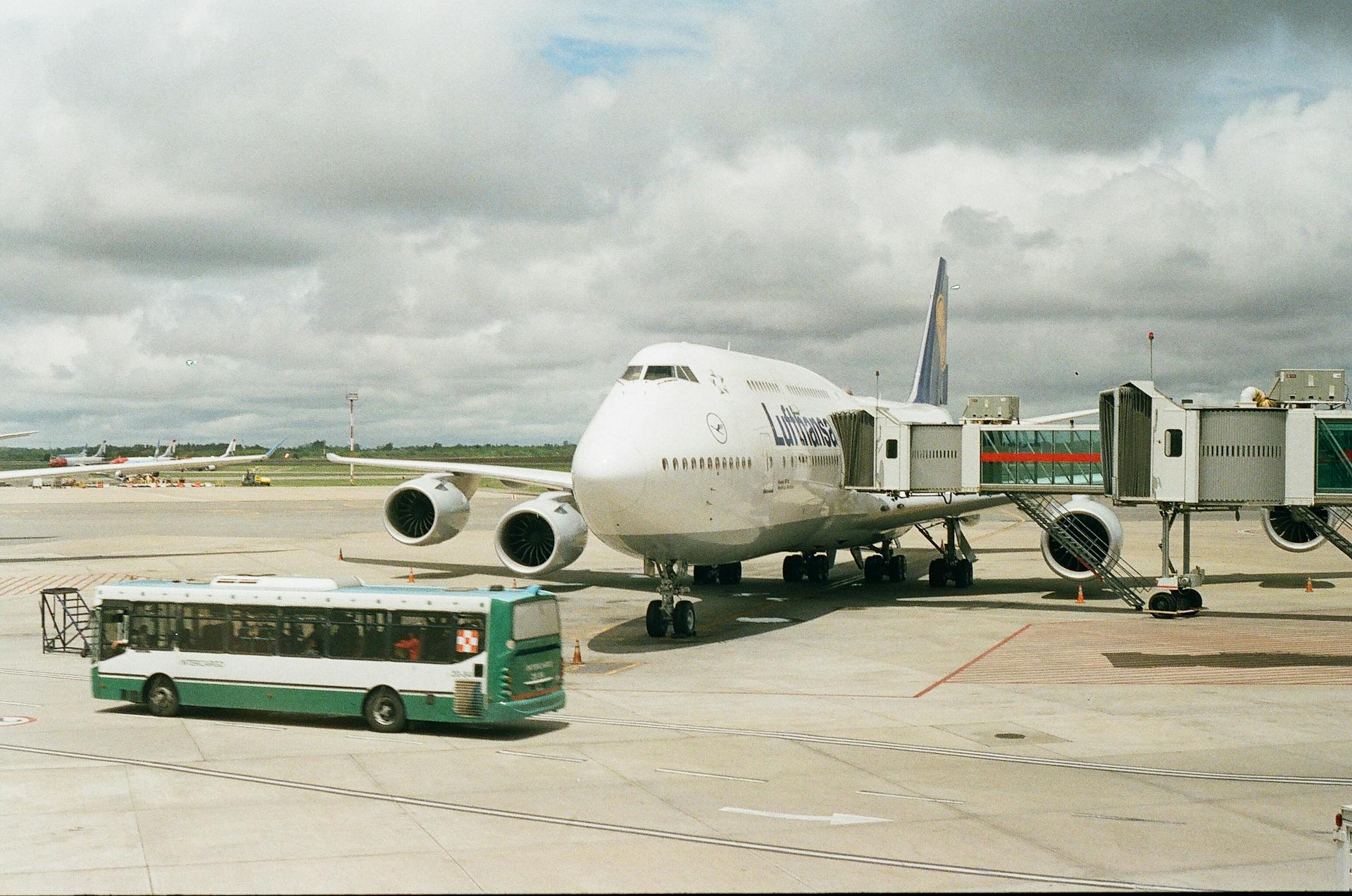 Plane on Airport with Telescopic Corridor Attached and Bus Driving in front of It