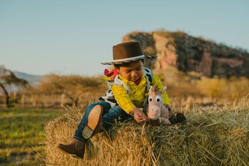 Photo of a Kid Sitting on Hay with a Stuffed Toy