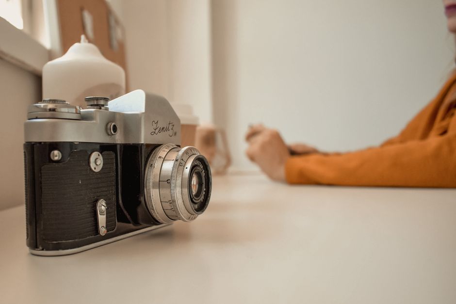 Close-up view of a vintage Zenit film camera on a table with a softly blurred figure in the background.