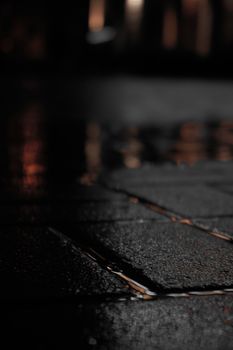 Close-up of wet pavement at night with blurred reflections creating a moody urban ambiance.