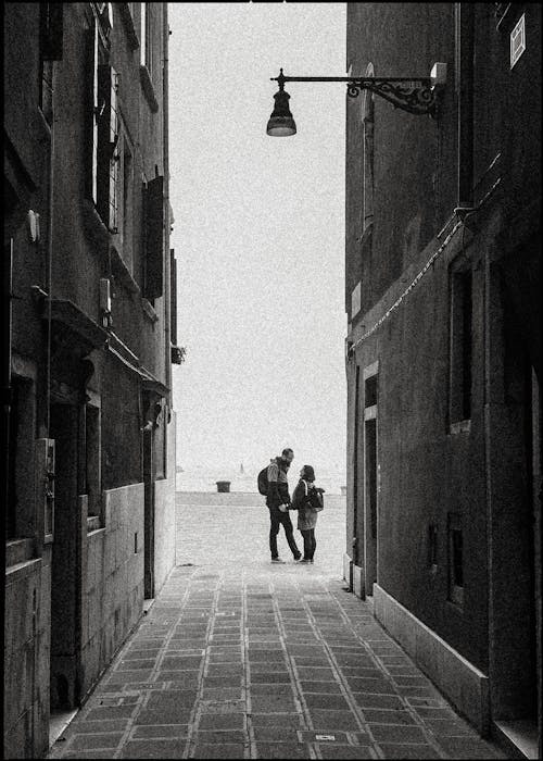 Grayscale of Man and Woman Standing Fae Each Other Near Buildings 