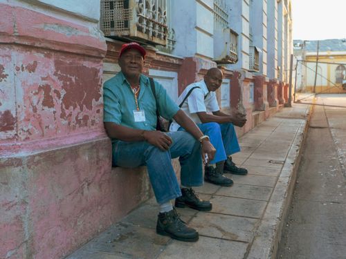 Free Two senior men sitting and smiling on a sidewalk, enjoying a sunny day. Stock Photo