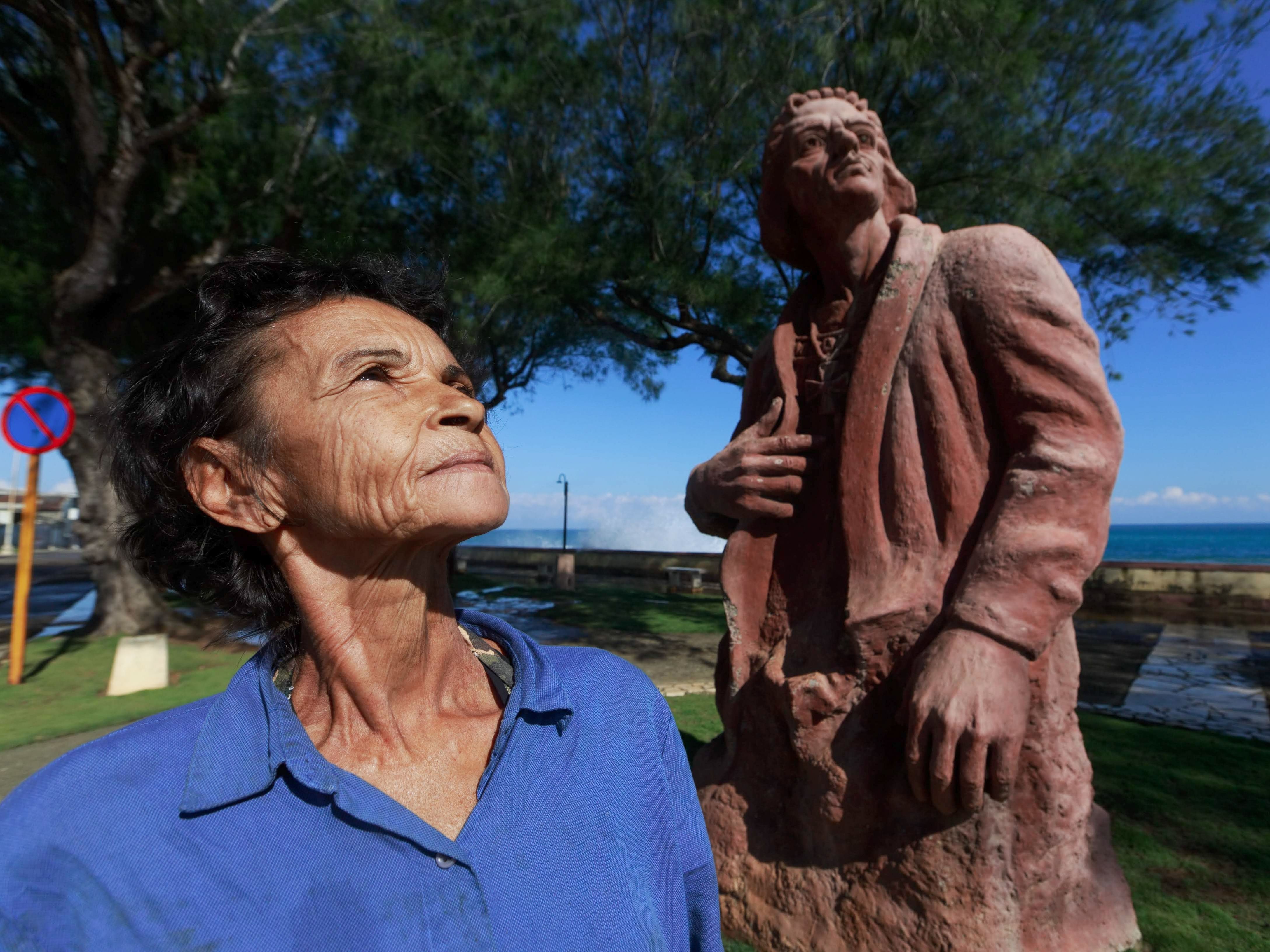 A senior woman looks up beside a stone sculpture in a scenic outdoor setting.