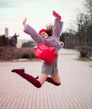 一位穿着充满活力服装和配饰的时尚年轻女性，在户外欢乐地跳跃