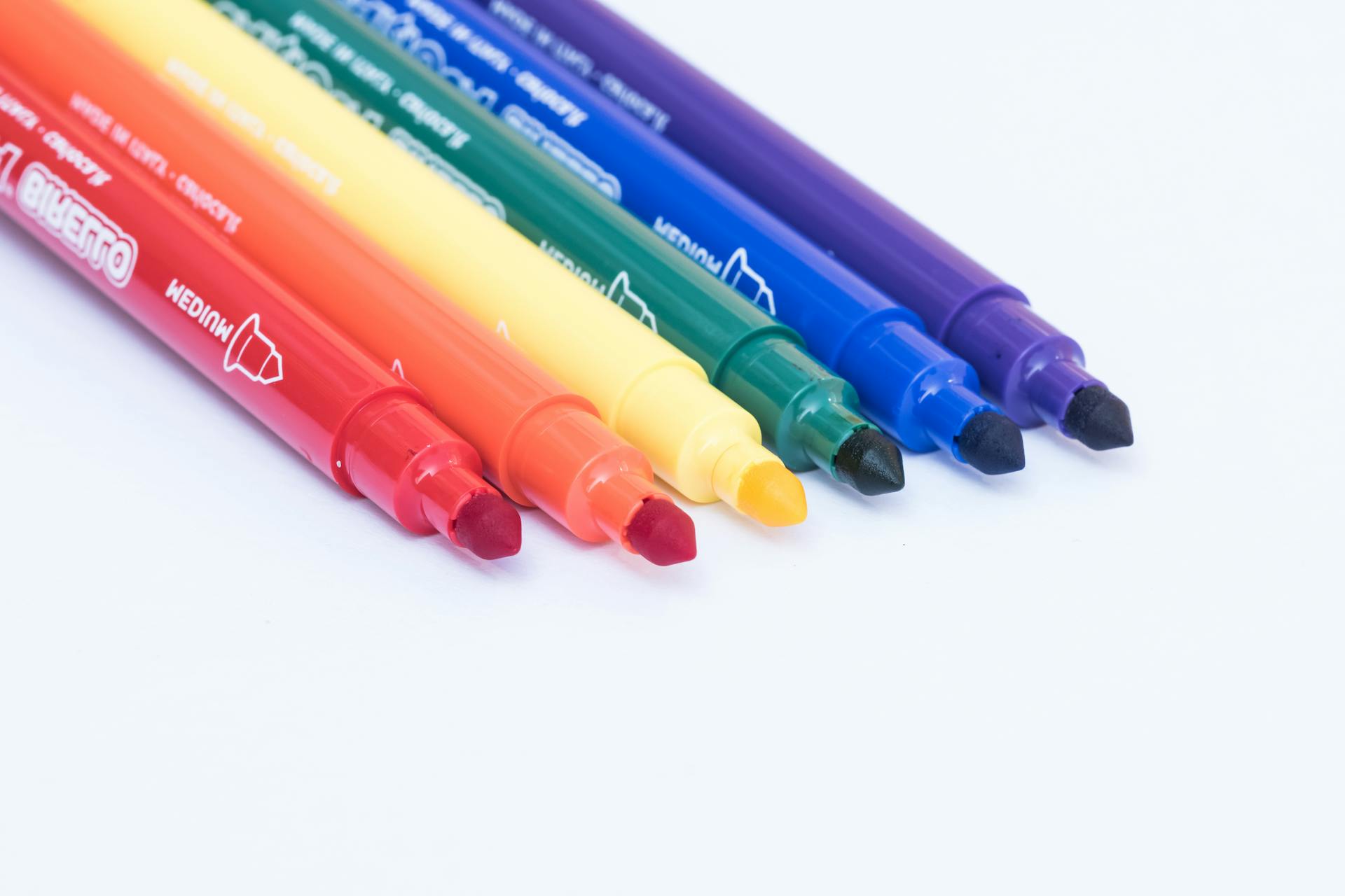 A close-up of six colorful markers arranged in a row, showcasing a spectrum of rainbow colors.