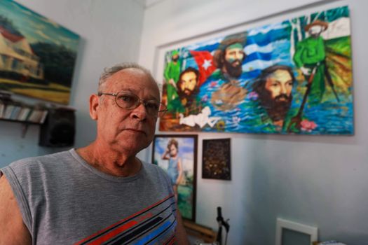 Elderly man with eyeglasses in art studio room with vibrant paintings.