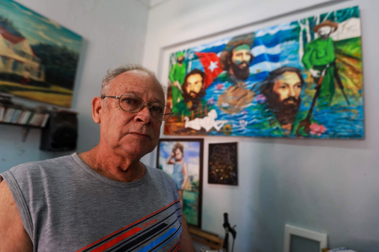 elderly man with eyeglasses in art studio room with vibrant paintings