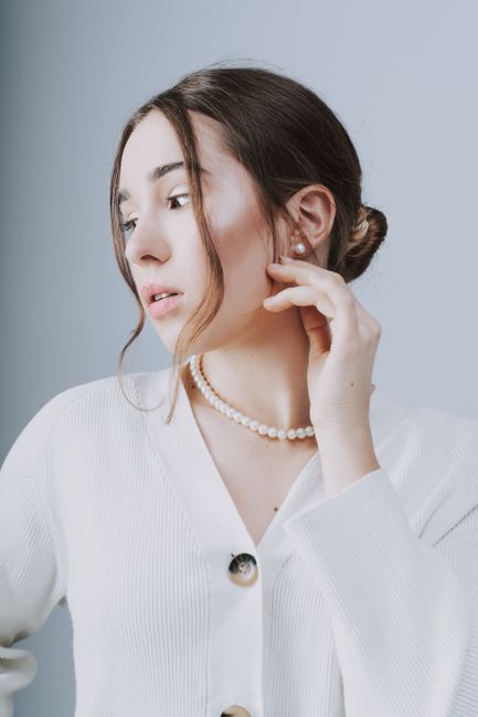 A refined portrait of a brunette woman with a pearl necklace and white cardigan, exuding elegance and simplicity.