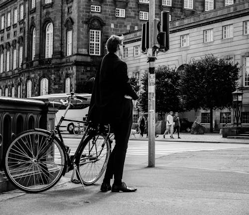 Free Man in Coat and Pants Standing Beside Bicycle on Road Stock Photo