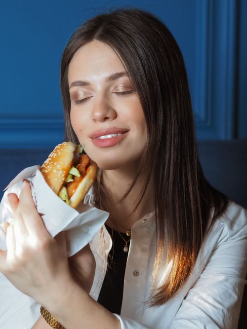 Free A woman savors a tasty hamburger with her eyes closed, creating a moment of enjoyment. Stock Photo