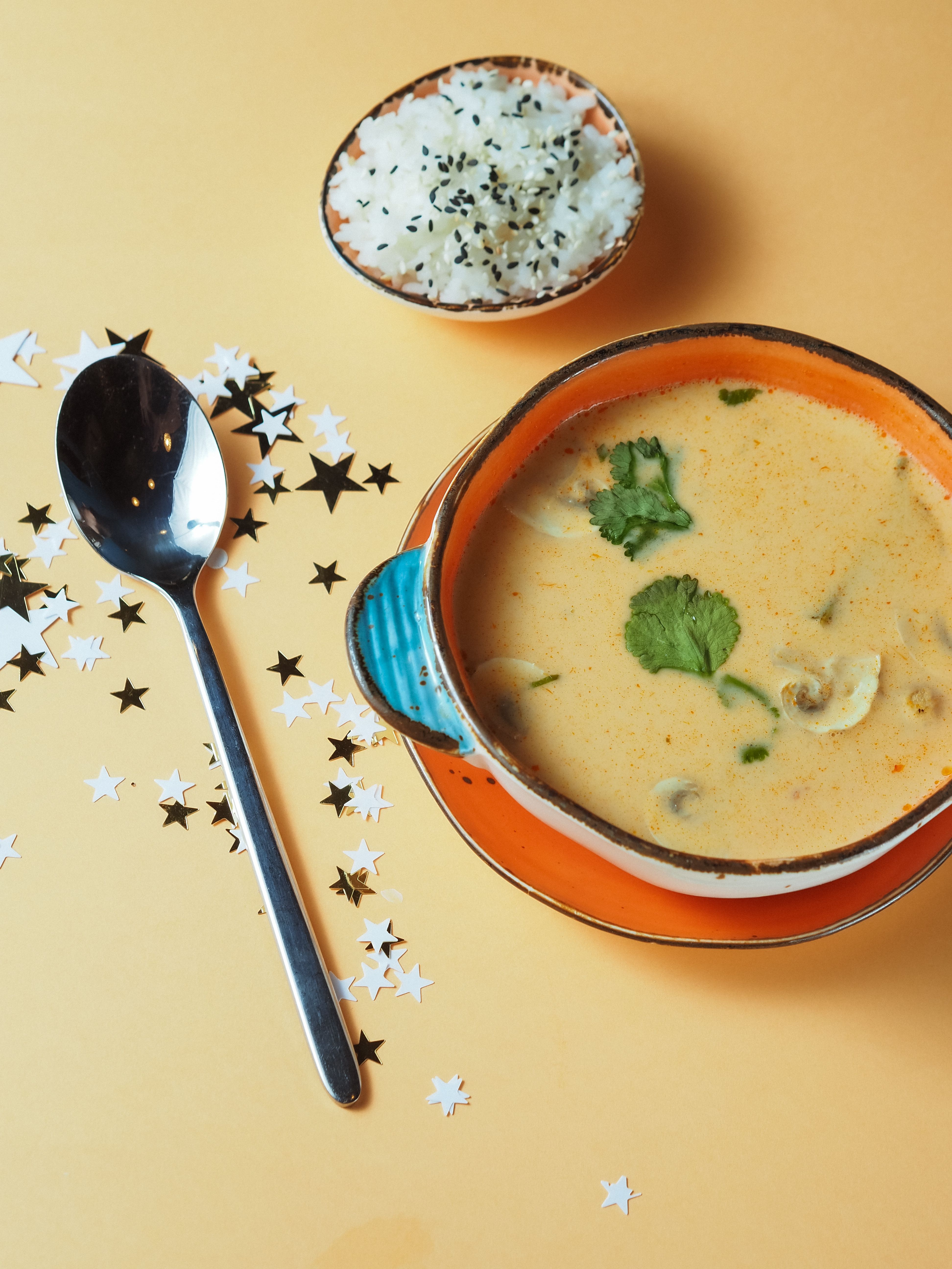 Delicious creamy soup garnished with herbs alongside rice on a yellow background.