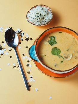 Delicious creamy soup garnished with herbs alongside rice on a yellow background.
