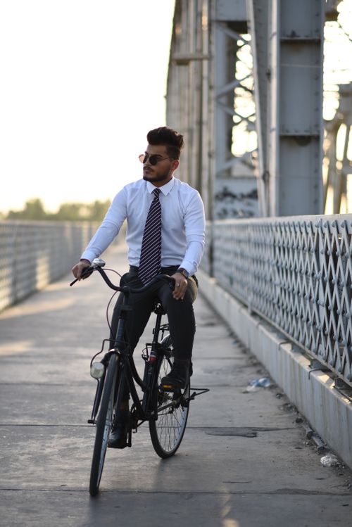 Free Man in office attire cycling over a bridge, combining business and eco-friendly transportation. Stock Photo