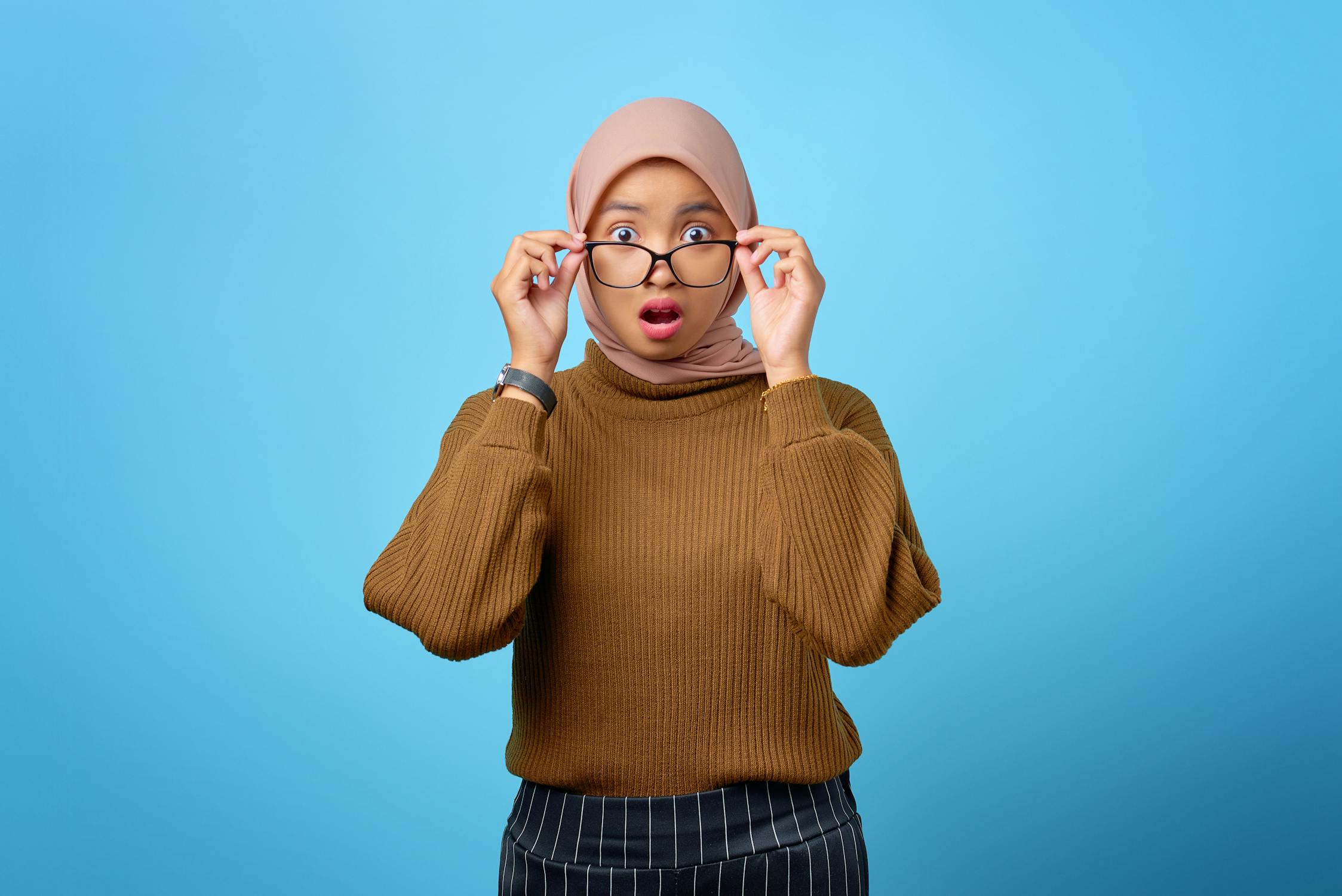 Woman in Brown Sweater Wearing Eyeglasses on Blue Background