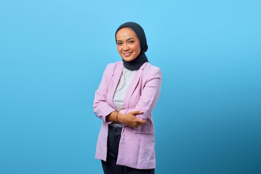 Portrait of a smiling woman in hijab and purple blazer against blue background.
