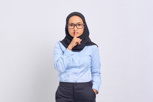 Free Asian Muslim woman in hijab making a quiet gesture with a serious expression, wearing eyeglasses against a white background. Stock Photo