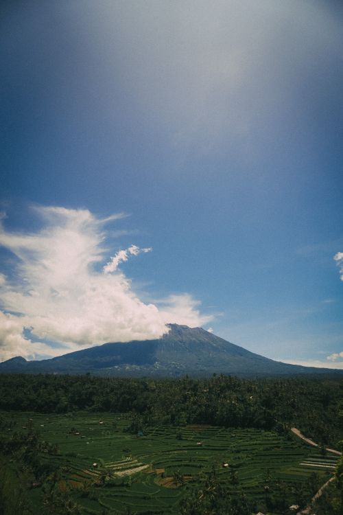 Free A breathtaking vertical shot of Mount Agung against a clear blue sky, surrounded by lush greenery and clouds. Stock Photo