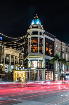 Iconic Beverly Hills building illuminated at night with motion blur from passing cars.