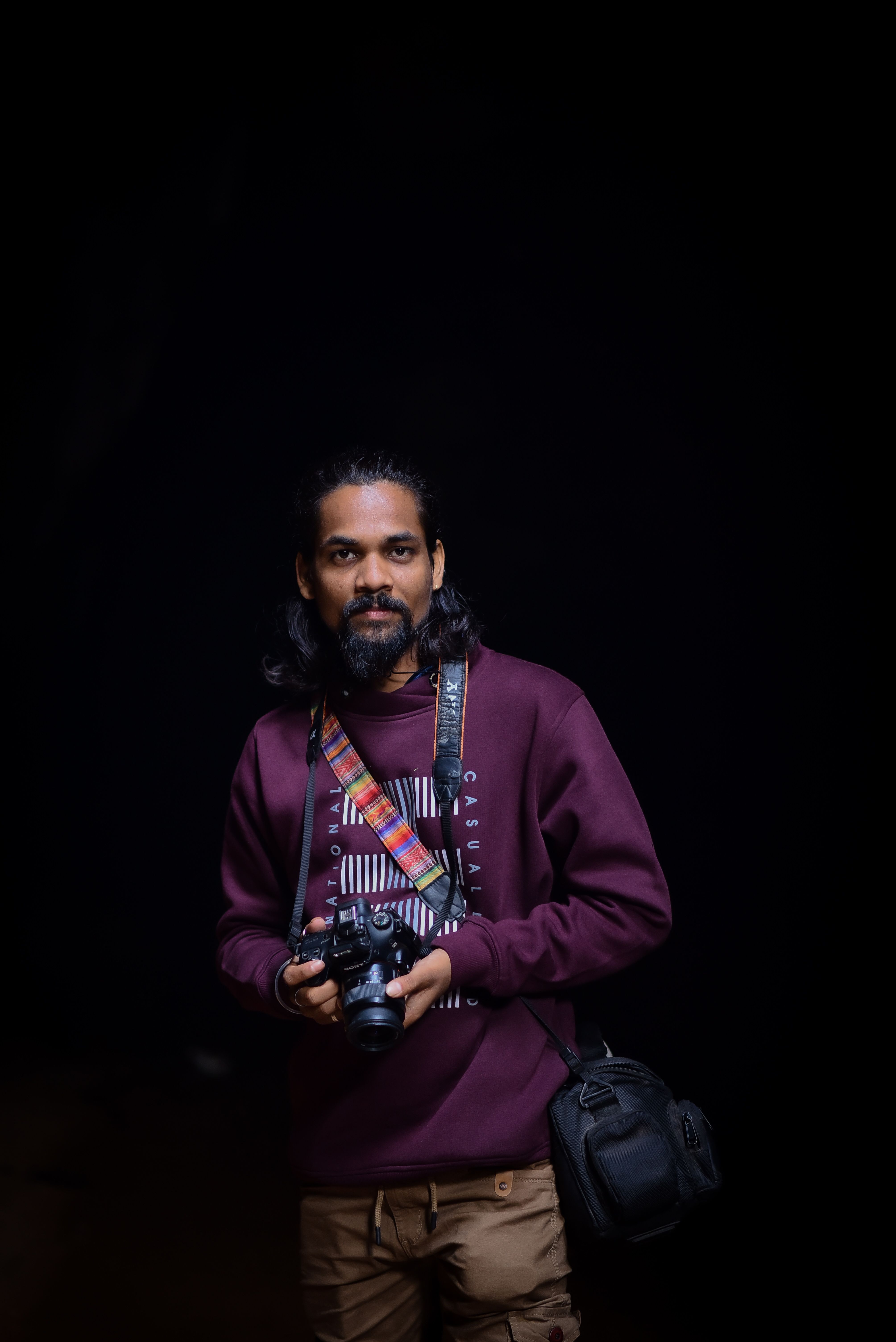 A photographer with long hair holding a camera against a black background, showcasing creativity.