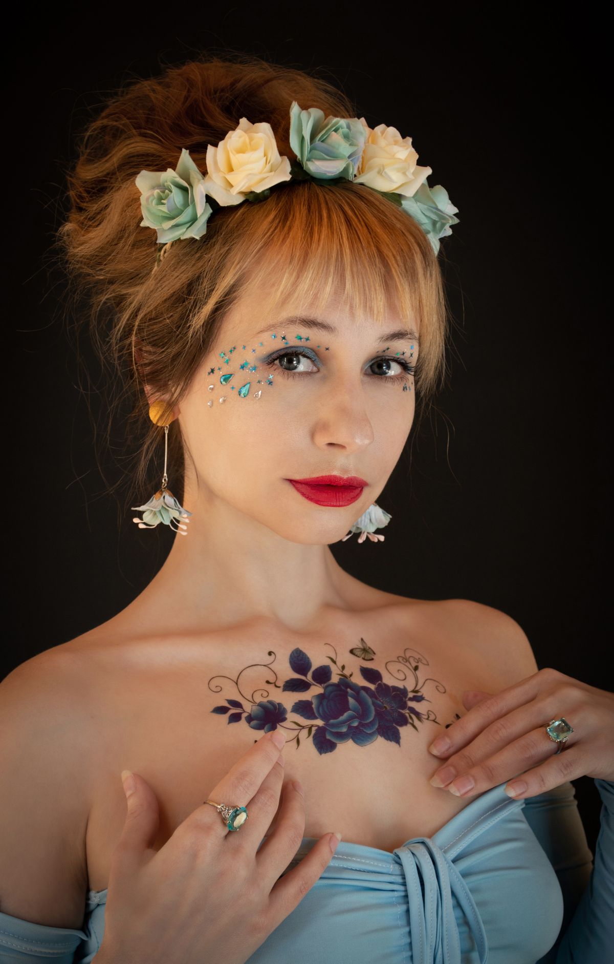 Portrait of a woman adorned with a floral crown, blue dress, and intricate tattoos on a dark background. Stock Photo.