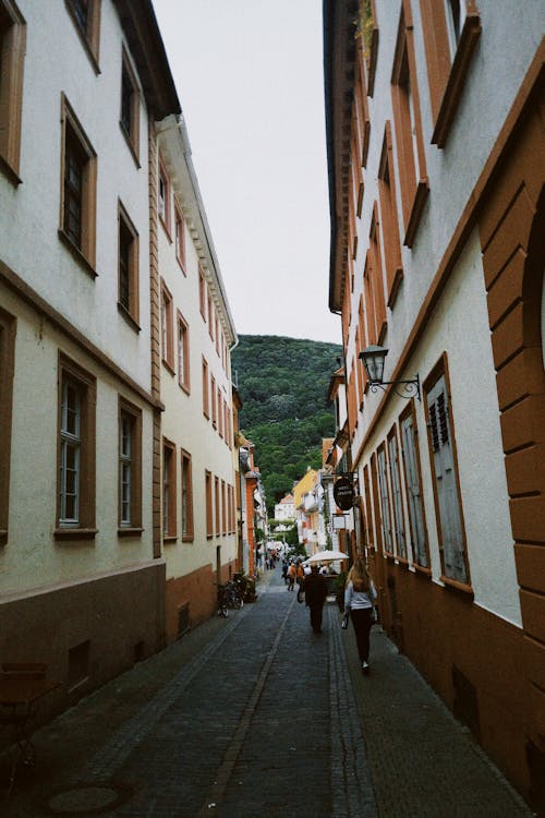 People Walking on Narrow Street between Concrete Buildings