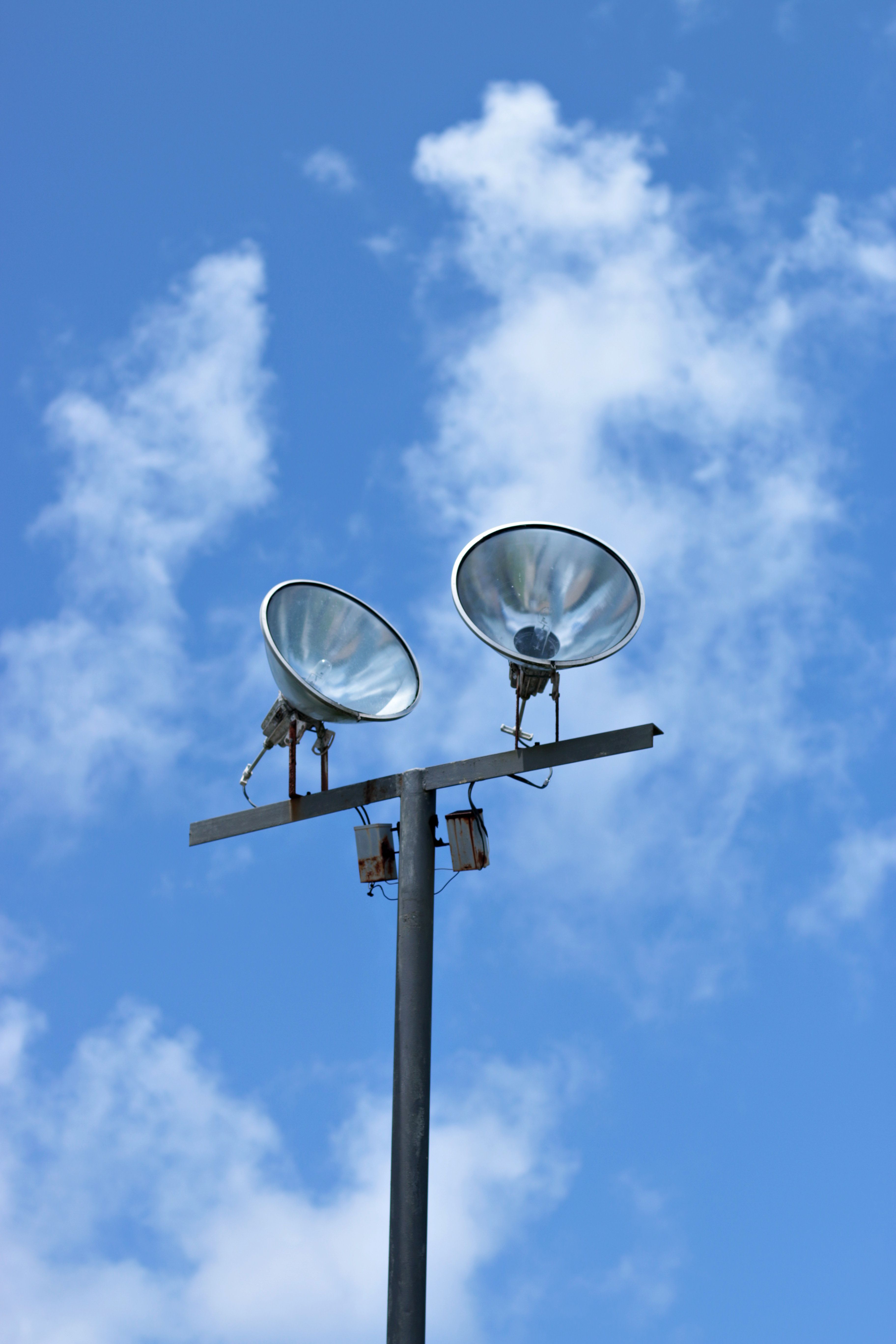 Two spotlights on a post with clouds and blue sky backdrop taken with Canon EOS 70D.