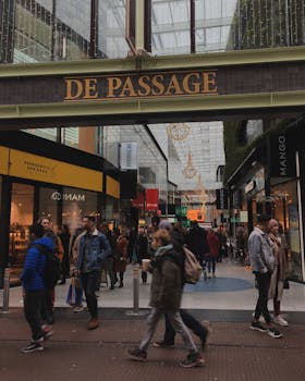 Lively scene at 'De Passage' shopping center with people walking and vibrant storefronts.