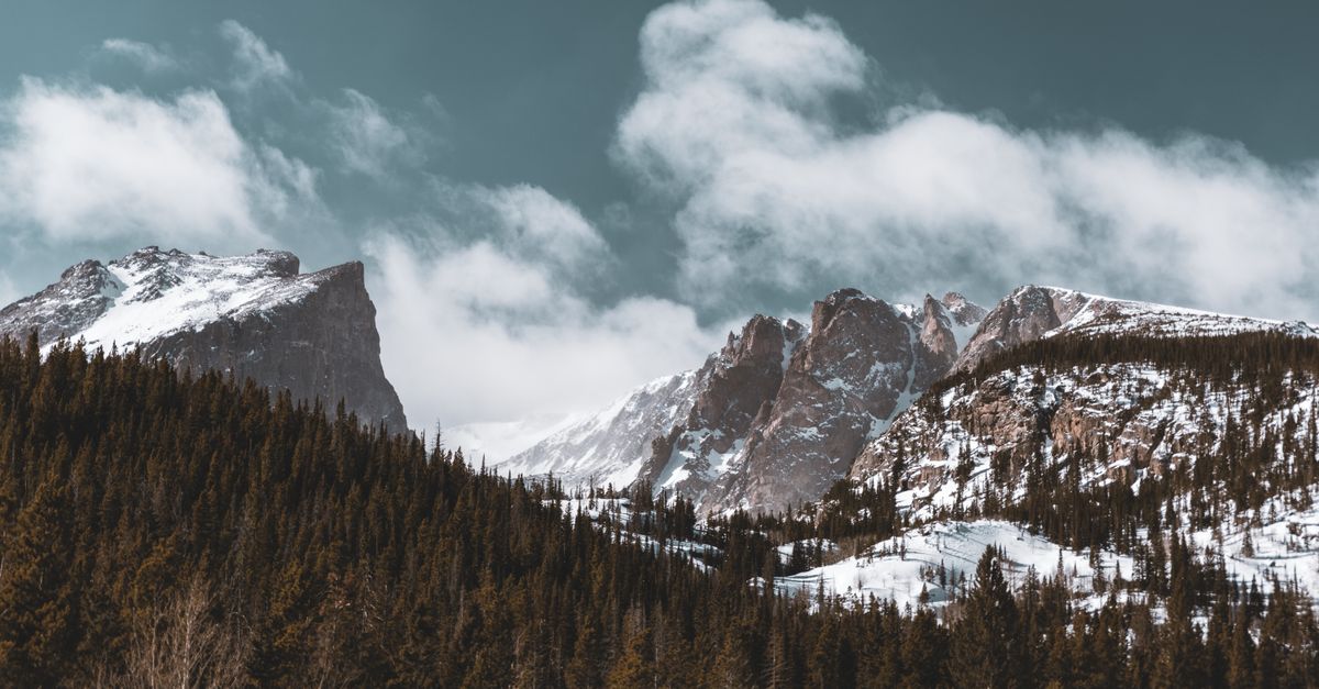 Snow-covered mountains and pine trees under a cloudy sky in Colorado's winter landscape.