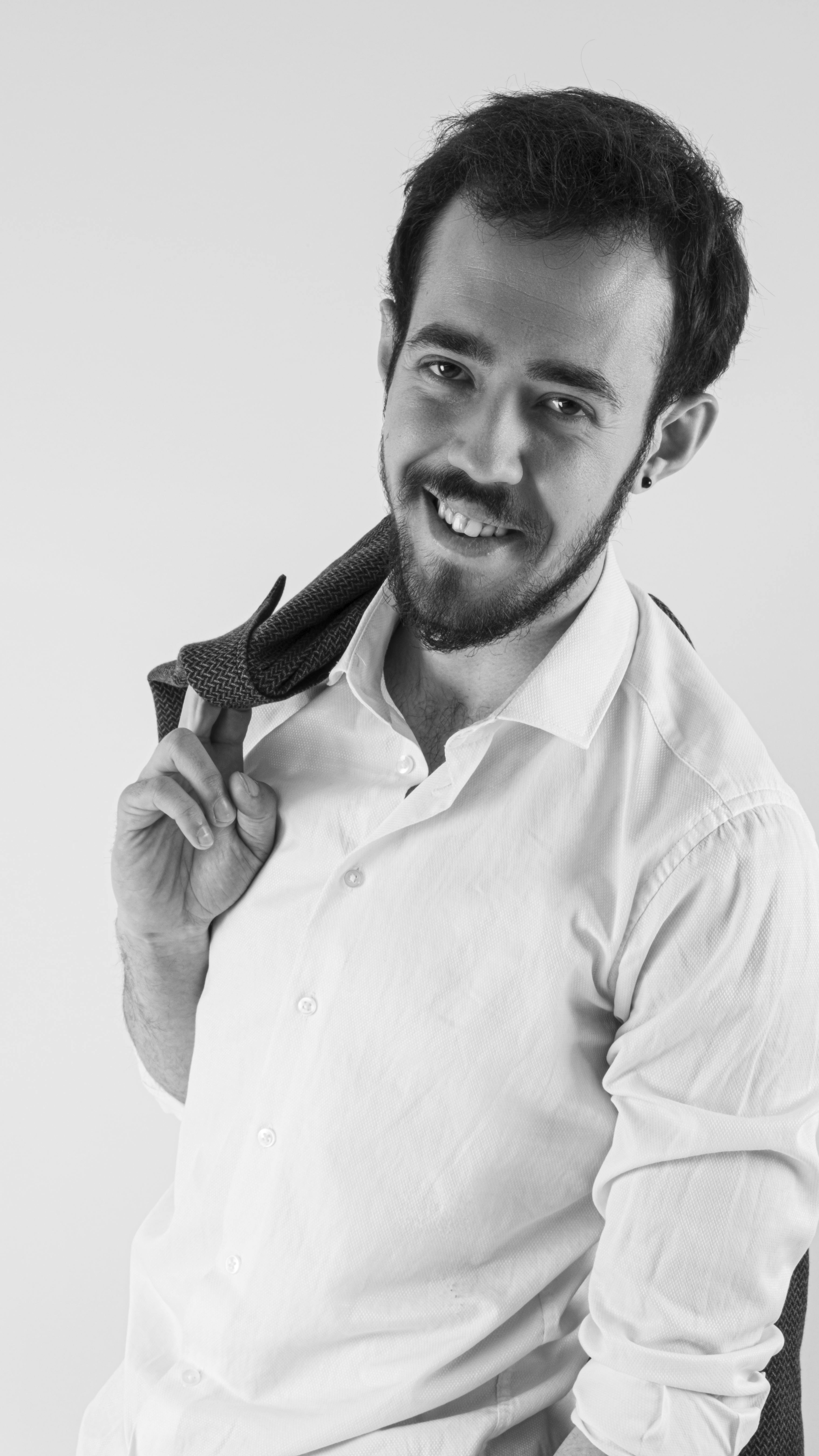 Grayscale portrait of a young man smiling, wearing a shirt and holding a tie over his shoulder.