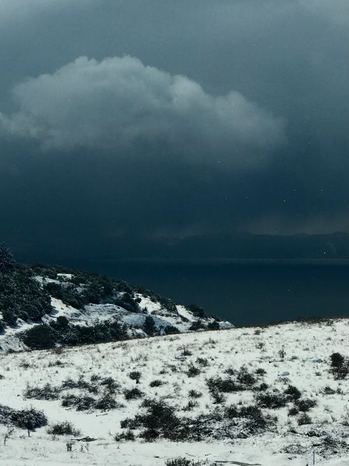 Free Moody winter landscape with snow-covered shore and dark clouds over water. Stock Photo
