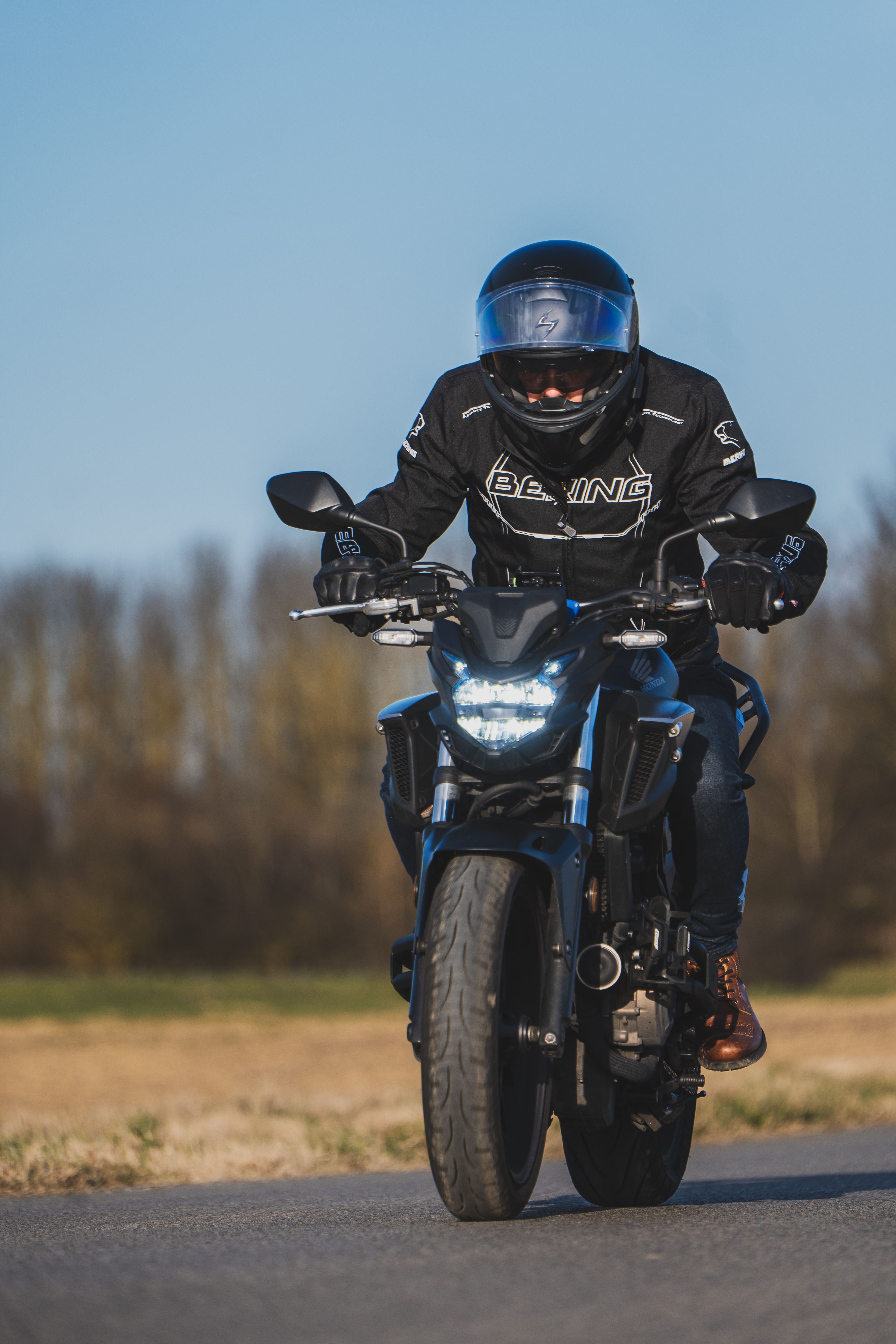 A motorcyclist in protective gear rides through the countryside on a sunny day.