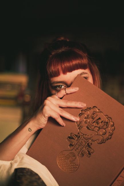 Mysterious portrait of a young woman with fringe hair partially hiding behind a book.