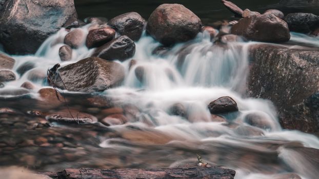 Peaceful long exposure of water running over rocks in a tranquil stream setting.