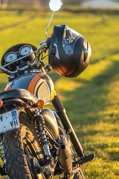 Close-up of a vintage motorcycle with a helmet on a sunny day in a green field.